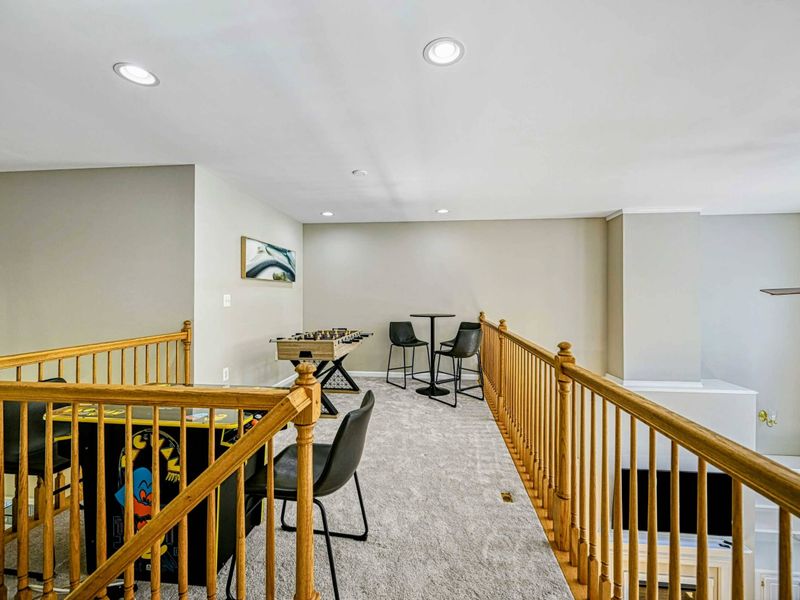 Loft Game Area - Upper-level landing with foosball table, bistro table, arcade game, and oak railing overlooking the great room.