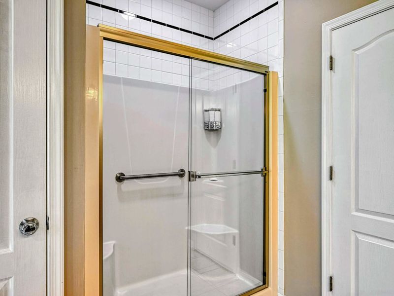 Primary Bathroom - Glass-door walk-in shower with white tile and grab bar beside the linen closet.