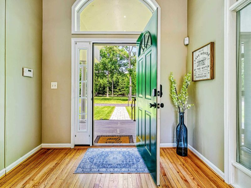 Foyer - Green front door with arched transom opens to hardwood floors, staircase, and lake house artwork.