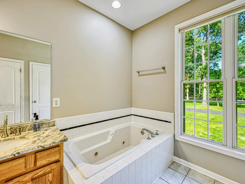 Primary Bathroom - Corner jetted soaking tub with white tile surround and large window overlooking the green yard.