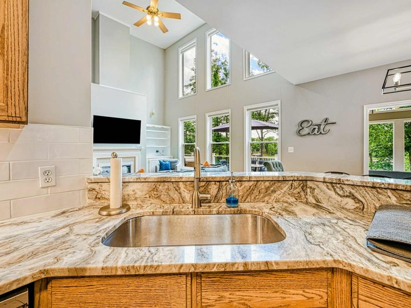 Kitchen - Island sink detail with sightline to the dining chandelier, living room TV, and tall windows beyond.