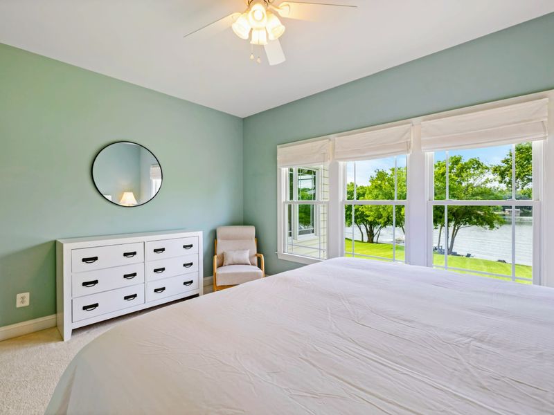 King Bedroom - The dresser side with a round mirror, reading chair, and lake views through the windows.