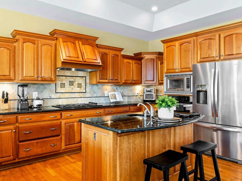Kitchen Island - A closer look at the granite-topped island with seating and the full suite of stainless appliances behind it.