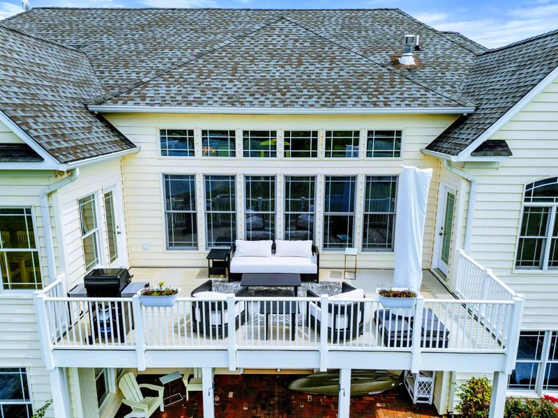 Upper Deck Aerial - The furnished upper deck with comfortable seating, a grill, and views across the lawn to the lake.