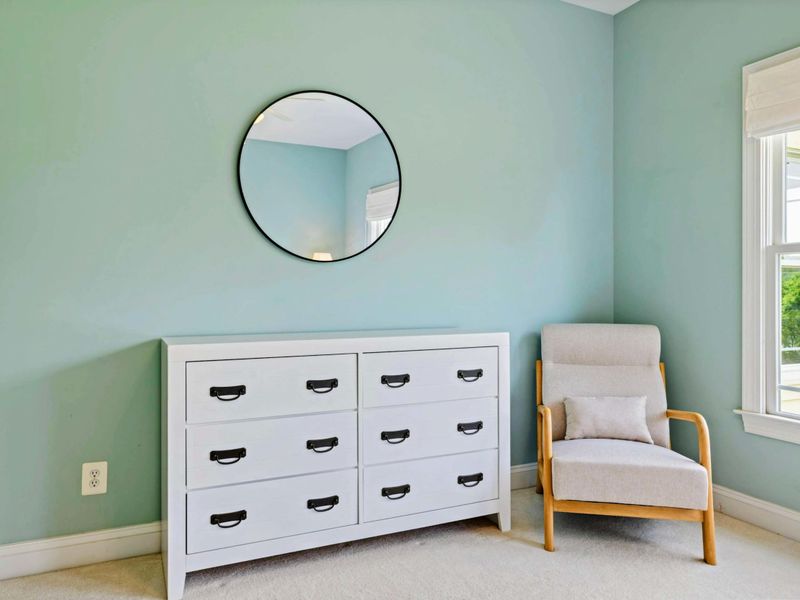 Bedroom Detail - A white dresser, round mirror, and reading chair in the sage guest room, with views of the yard.