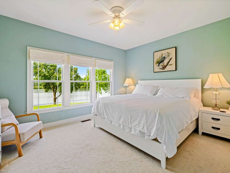 King Bedroom - Soft sage walls, a white king bed, heron art, and lake views through large windows create a peaceful guest room.