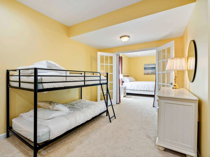 Bunk Room - Looking through to the adjoining queen suite, with a dresser and reading lamp framing the French door passage.