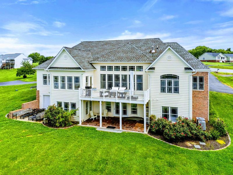 Rear Aerial - A bird's-eye view showing the expansive deck, walkout patio, and landscaped yard leading to the water.