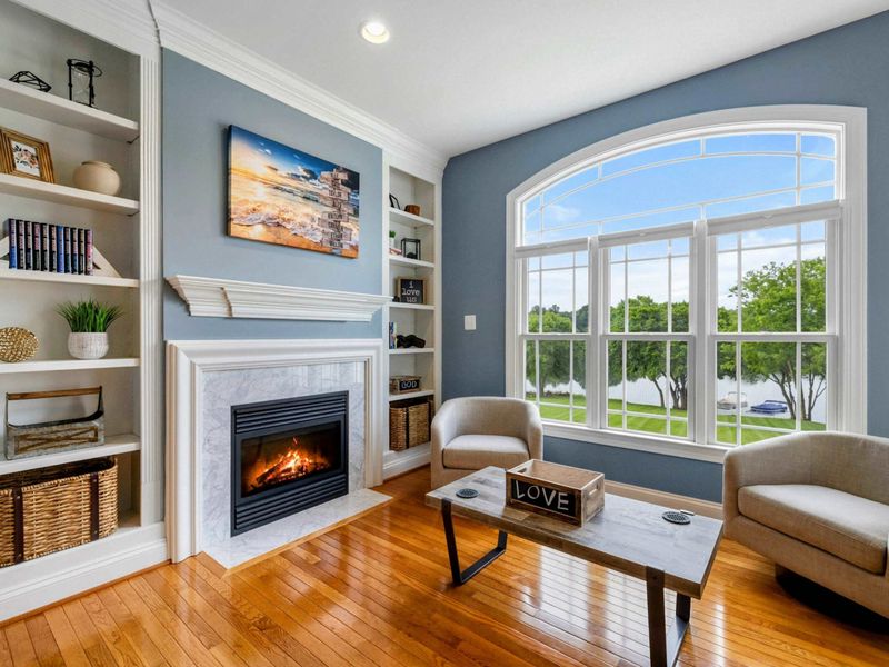 Primary Fireplace Detail - Built-in bookshelves, a beach painting, and a marble-surround fireplace with the lake visible through the window.