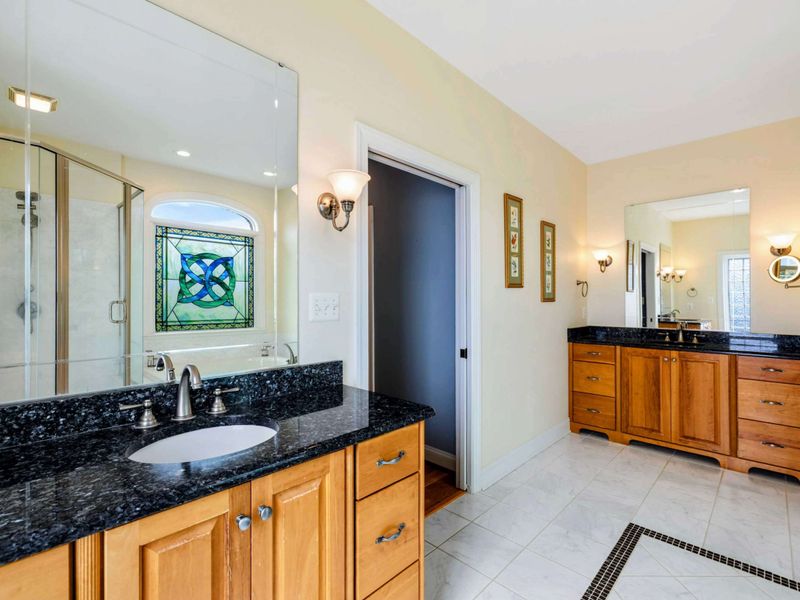 Double Vanity - Two separate vanities with black granite, warm wood cabinetry, and sconce lighting in the primary ensuite.