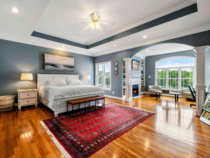 Primary Suite - A king bed, tray ceiling, hardwood floors, and an arched sitting area with fireplace make this the most private retreat in the house.