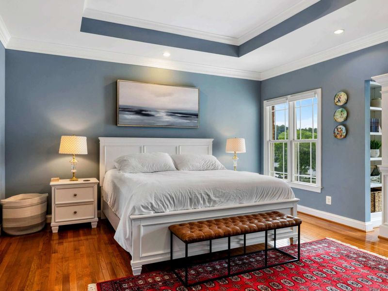 Primary Suite - The king bed with a tufted leather bench, ocean art, and a view through the arch to the sitting area beyond.