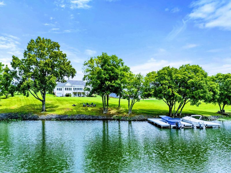 Lakefront Approach - A closer look from the water reveals the dock, boat lift, and the home rising above the tree-lined shore.