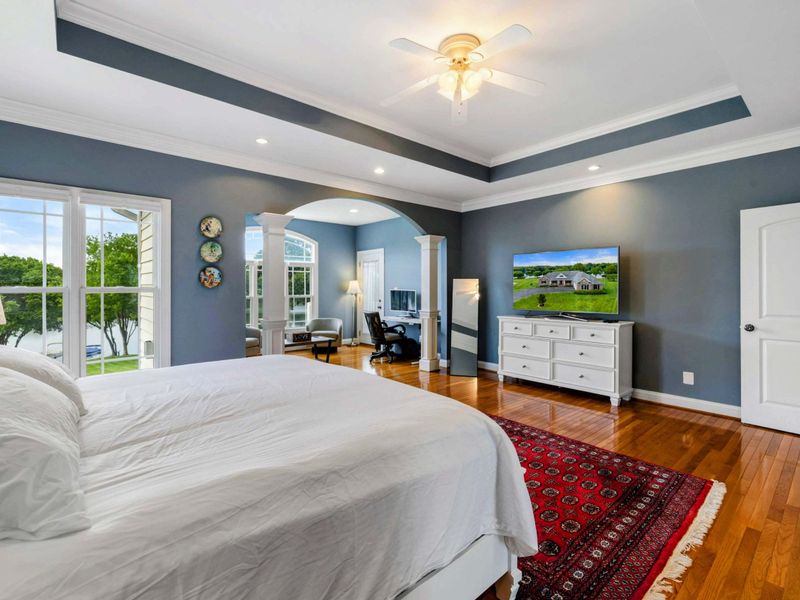 Primary Suite - From the bed, the TV, dresser, arched sitting area, and lake views through the windows are all in view.