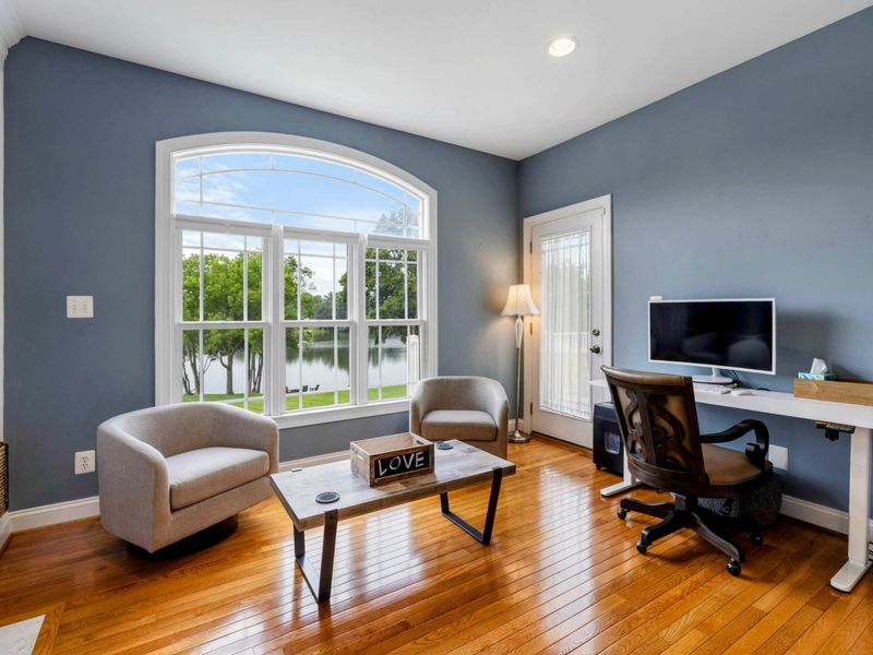 Primary Sitting Area - A standing desk, accent chairs, and a fireplace with lake views through the arched window, ideal for remote work or quiet mornings.