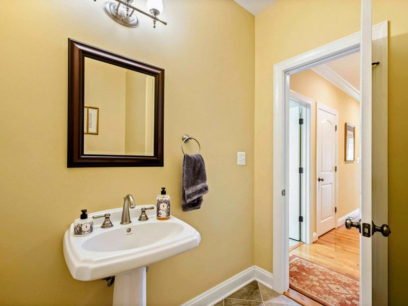 Powder Room - A pedestal sink with a dark-framed mirror in warm yellow tones provides a convenient half bath on the main level.