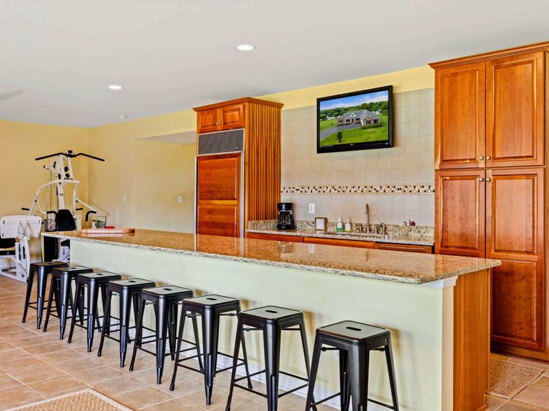 Wet Bar Close-Up - Granite countertops, a Smart TV, Subzero fridge, coffee maker, and tile backsplash behind the bar.