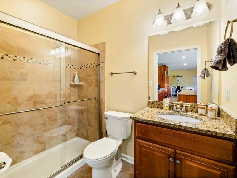Lower Bath - A full bath with a glass-enclosed tub and shower combo, granite vanity, and warm tile finishes.