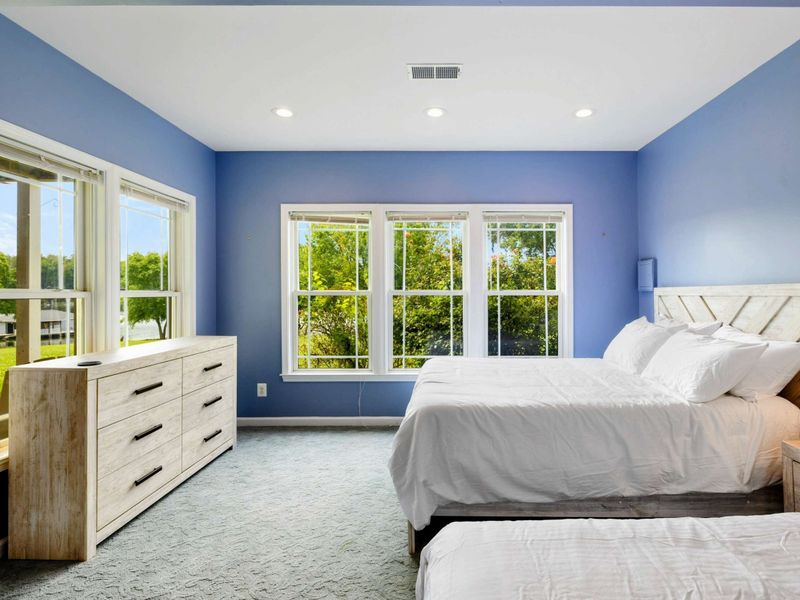Double Queen Bedroom - A dresser with mirror anchors the room, while two sets of windows frame views of the yard and lake beyond.