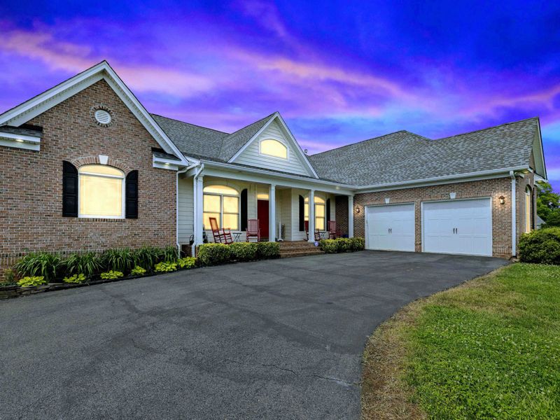 Welcome Home - The brick facade, covered porch with rocking chairs, and red front door glow warmly at dusk, setting the tone for a memorable stay.