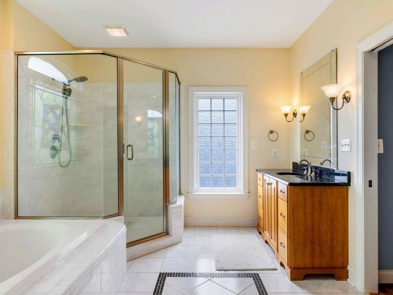 Shower and Vanity - The glass-enclosed shower and single vanity with black granite, sconce lighting, and marble floor tile.