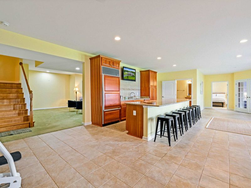 Lower Level Bar - The wet bar with Subzero fridge, barstool seating for eight, a Smart TV, and the staircase to the main level.