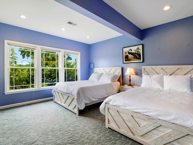 Double Queen Bedroom - Two white farmhouse-style queen beds sit beneath a tray ceiling with heron artwork, perfect for friends or family sharing a room.