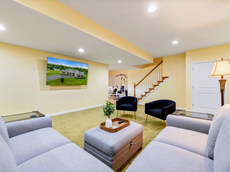 Game Room TV - The big-screen Smart TV and sectional sofa, with the staircase, bar, and home gym nearby.