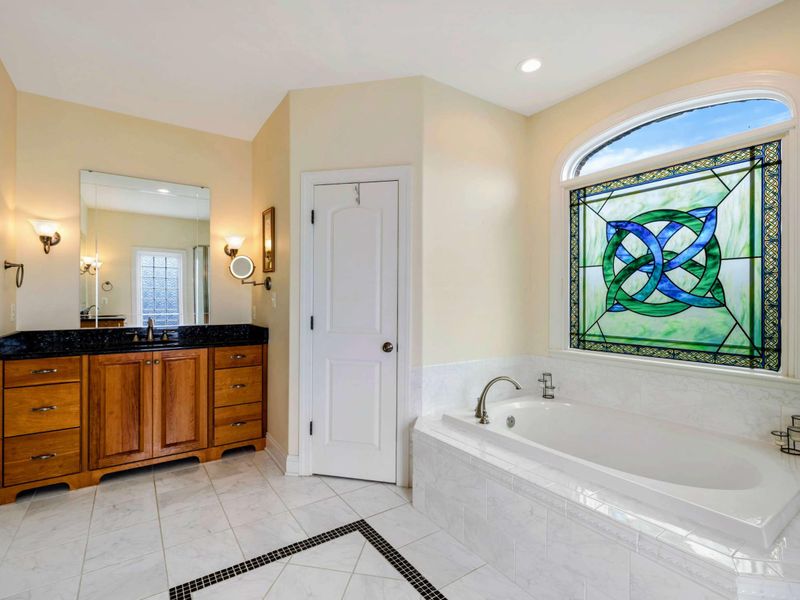 Primary Ensuite - The double vanity with black granite countertops, a soaking tub with stained glass, and the walk-in closet beyond.