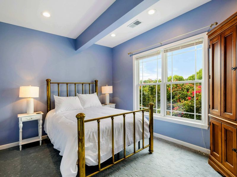 Lower Bedroom - Soft periwinkle walls, a brass bed frame, and a garden view window make this queen room a quiet retreat on the lower level.