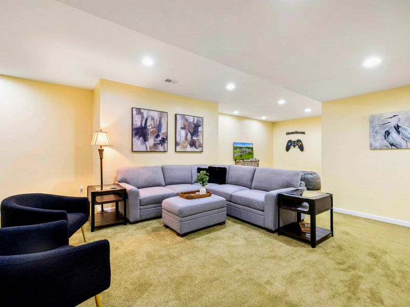 Game Room - A wide view showing the sectional, accent chairs, art, and the "Game Room" sign, with a heron print on the far wall.