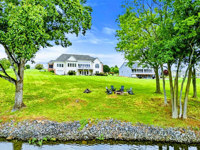 Waterfront View - The home and its green lawn seen from the shoreline, with the dock and water just steps away.