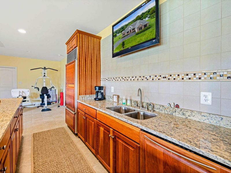 Bar Detail - The sink, granite counters, and tile backsplash with the home gym visible just beyond the bar area.