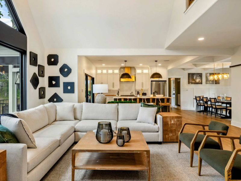 Great Room - Floor-to-ceiling windows fill the space with natural light while the open kitchen and dining area flow beyond.