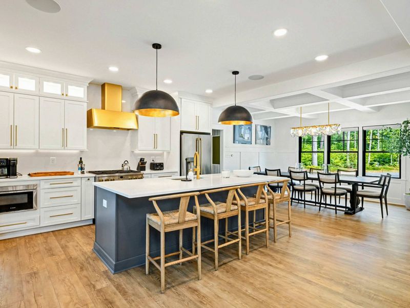 Kitchen - An open layout connects the island and cooking area to the dining room, with large windows framing the greenery outside.