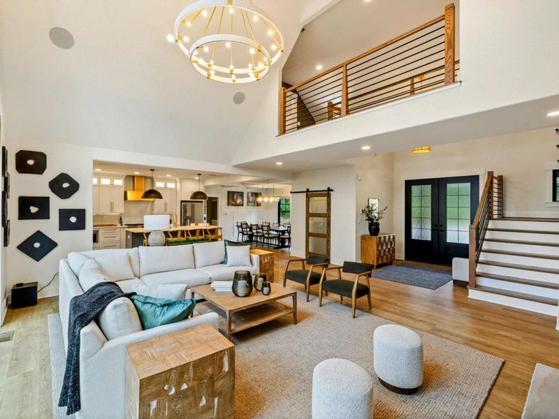 Great Room - Soaring A-frame ceilings, a gold chandelier, and a loft railing above create a grand open living space.