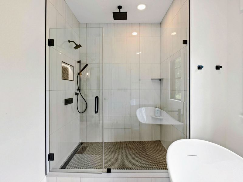 Primary Bathroom - An oversized walk-in shower features a rain showerhead, handheld sprayer, built-in bench, and glass enclosure.