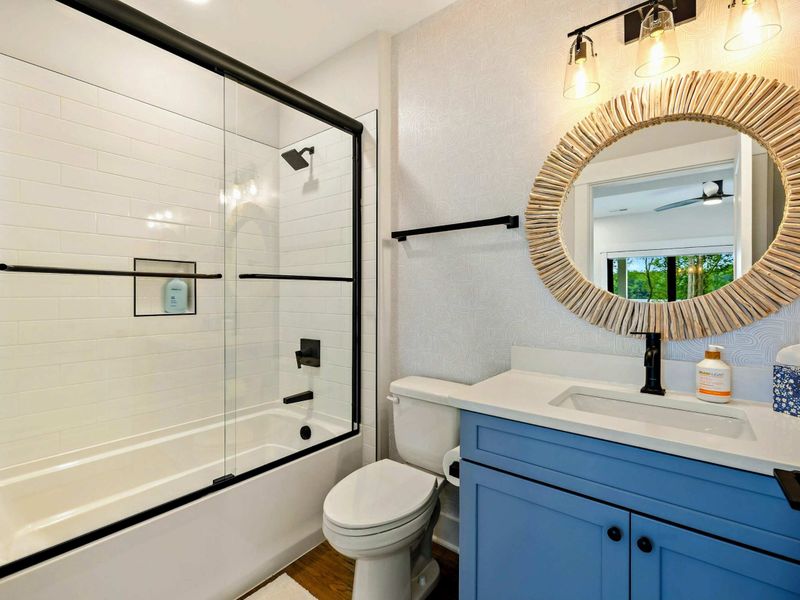 Bathroom 2 - A tub-shower combo with glass door, blue vanity, and driftwood-framed round mirror add coastal charm.