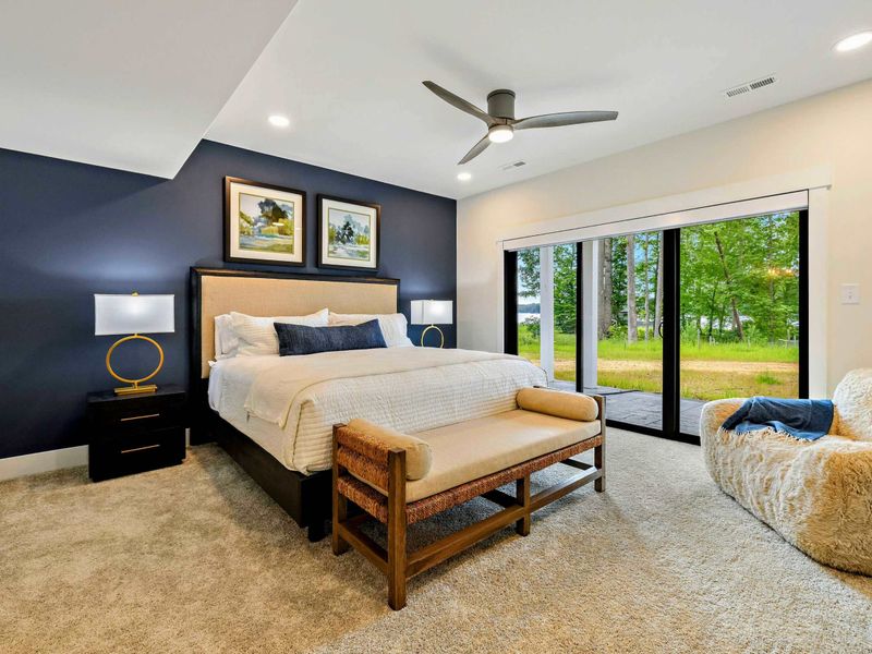 Bedroom 2 - A king bed with a navy accent wall, gold ring lamps, and sliding glass doors to the lakefront patio.