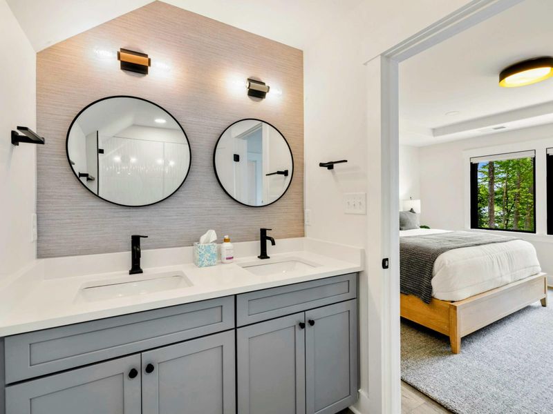 Bathroom 5 - A double vanity with gray cabinets, round mirrors, and grasscloth wallpaper accent connects to the king bedroom.