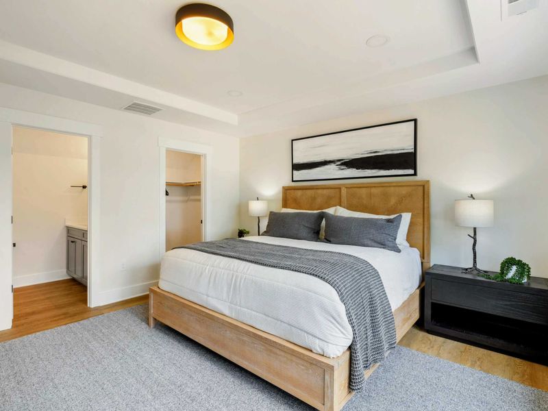 Bedroom 5 - A king bed with a natural wood frame, abstract landscape art, and a warm flush-mount light create an inviting main-level suite.