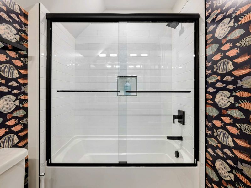 Jack-and-Jill Bathroom - A tub-shower combo with glass sliding door is framed by the colorful fish-print wallpaper.