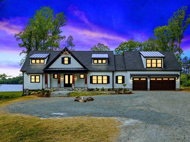 Front Exterior - At twilight, warm interior light glows through the windows of this striking modern farmhouse with metal roof dormers.