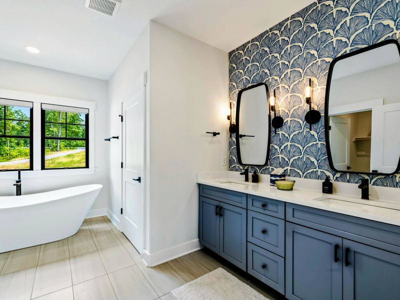 Primary Bathroom - A freestanding soaking tub sits beneath windows with garden views, complemented by the ginkgo leaf wallpaper and blue vanity.