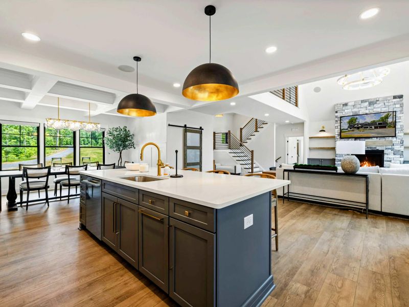 Kitchen - From behind the island, the open floor plan reveals the stone fireplace, living area, and soaring A-frame windows.