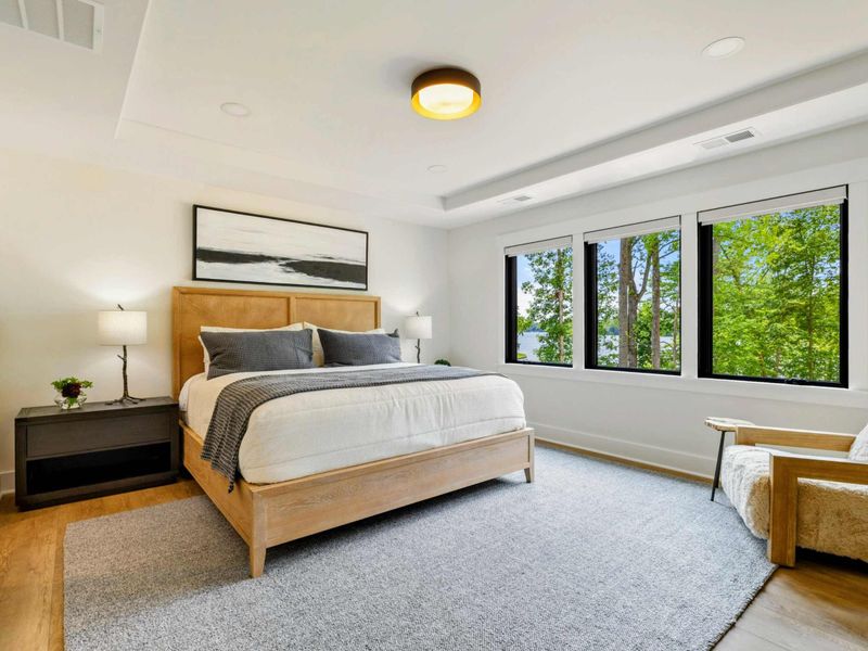 Bedroom 4 - A king bed with a natural wood frame faces three windows with filtered views of the lake through the trees.