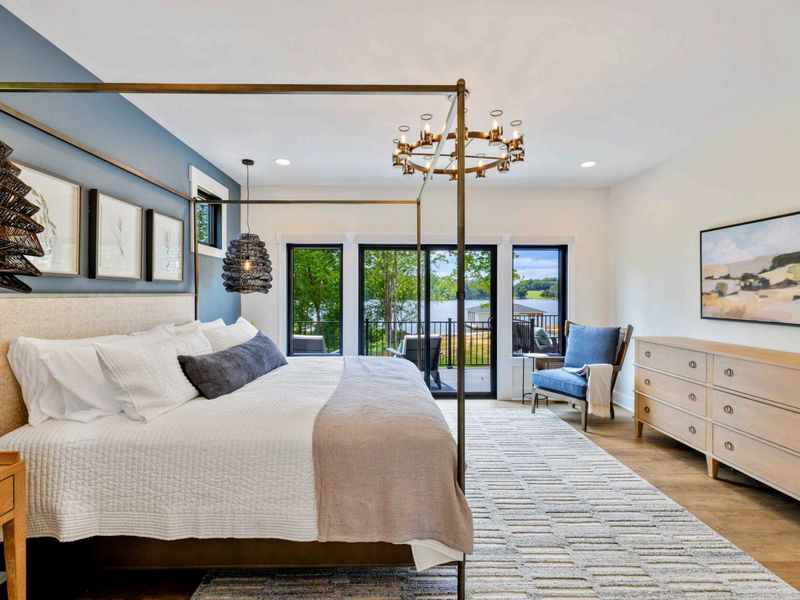 Primary Suite - Wake up to lake views through floor-to-ceiling sliders, with a plush reading chair and elegant dresser nearby.