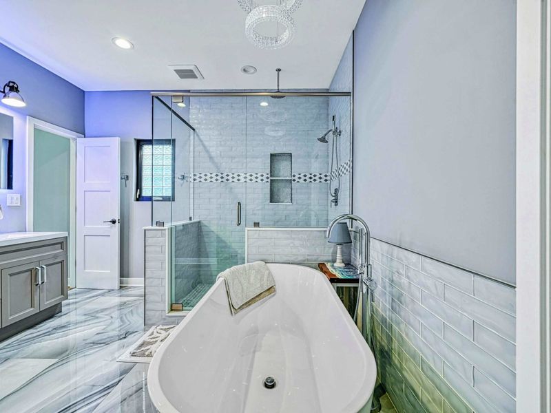 Soaking Tub Detail - The freestanding tub with chrome fixtures, a crystal chandelier above, and the glass-enclosed walk-in shower just beyond.