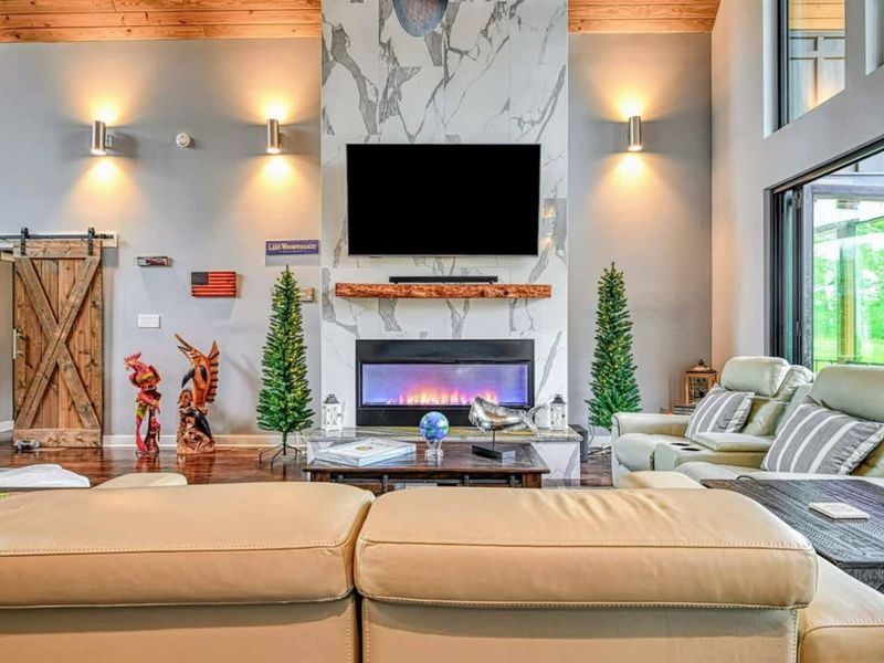 Fireplace Detail - A close-up of the floor-to-ceiling marble electric fireplace with a live-edge wood mantel, Smart TV, and warm wall sconces.