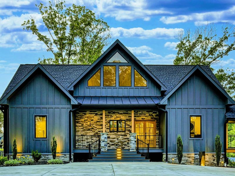 Twilight Front - The front facade at dusk, with warm light glowing through the A-frame peak, stone entry, and landscape uplighting.